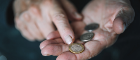 Two elderly hands cupping a few coins, with a copper-colored coin resting on the palm in focus.