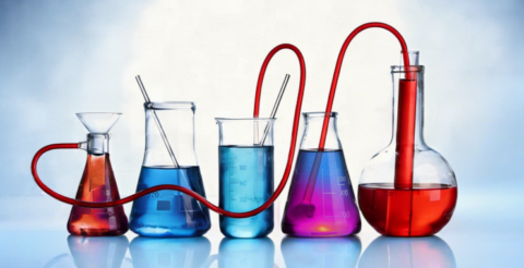 Series of laboratory glassware with colorful liquids connected by red tubing, forming a liquid transfer setup.