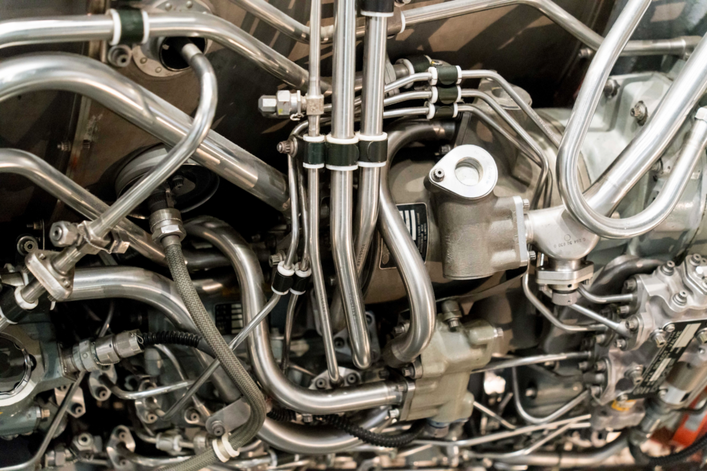 Close-up of a dense network of chrome-plated tubes, fittings, and clamps inside a mechanical engine compartment (likely aircraft or industrial turbine).